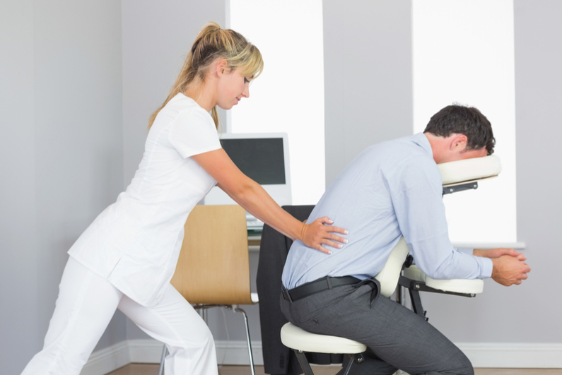 Masseuse treating clients lower back in massage chair