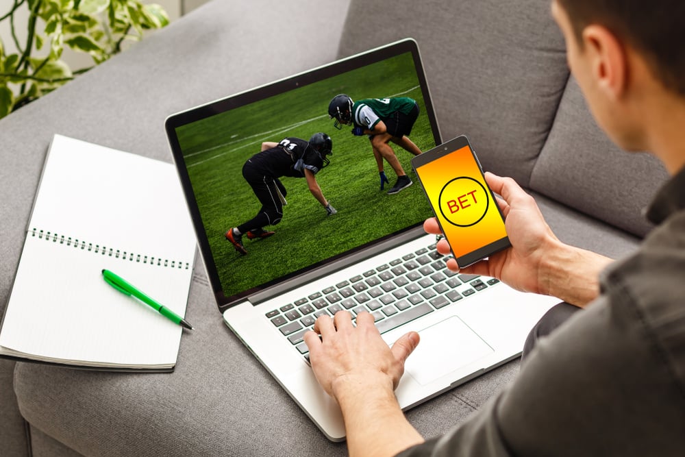 man betting on football using mobile and laptop