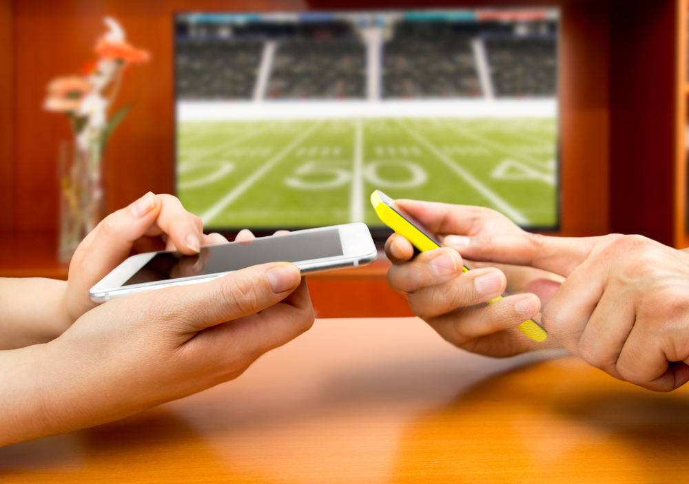 two people bet on their cell phones as a laptop screen shows an American football pitch