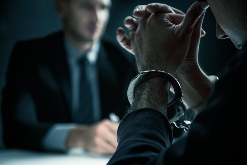 Man in handcuffs sits opposite an attorney